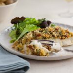herb crusted cod portion on plate broken with a fork.