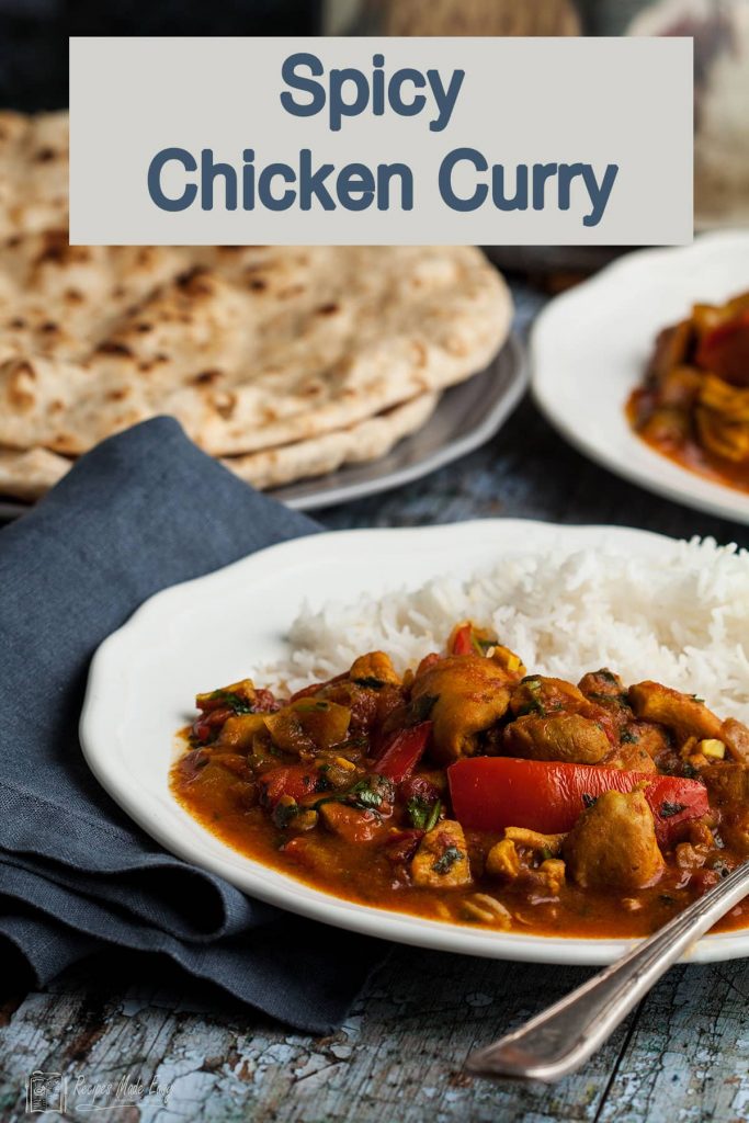 plate of spicy chicken curry with chapatis in the back ground.